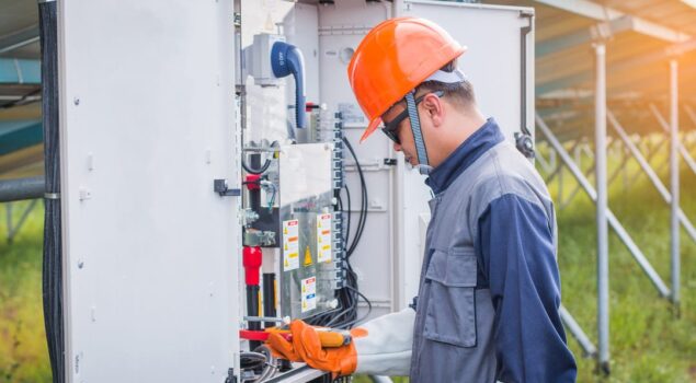 Profissional realiza inspeção em painel elétrico durante a Parada Anual de Manutenção Elétrica (PAME), utilizando equipamentos de proteção em área externa.