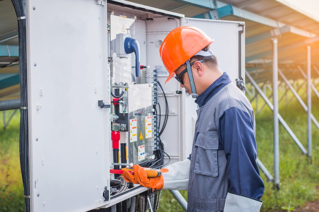 Profissional realiza inspeção em painel elétrico durante a Parada Anual de Manutenção Elétrica (PAME), utilizando equipamentos de proteção em área externa.