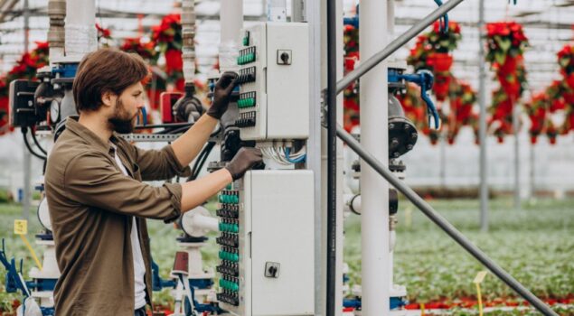 Técnico ajustando painel elétrico em estufa agrícola, realizando manutenção ou modernização de sistemas de irrigação.