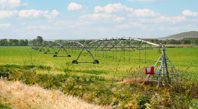 Sistema de irrigação por pivô central em plantação verde sob céu com nuvens.