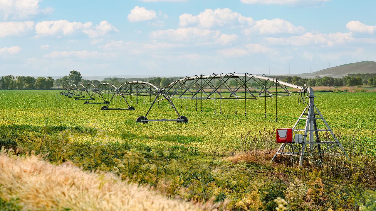 Sistema de irrigação por pivô central em plantação verde sob céu com nuvens.