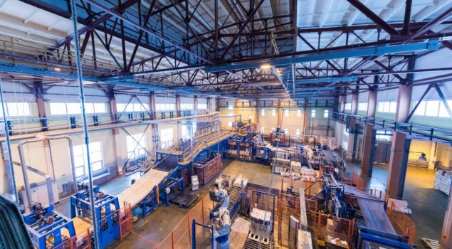 Vista ampla de uma fábrica com máquinas industriais, esteiras e linhas de produção em funcionamento.