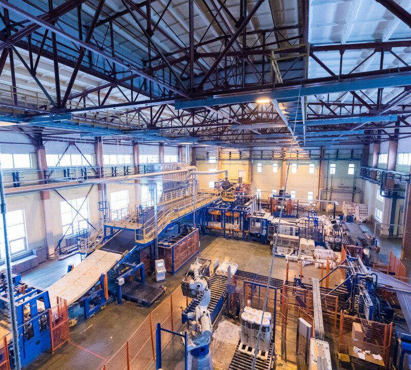 Vista ampla de uma fábrica com máquinas industriais, esteiras e linhas de produção em funcionamento.