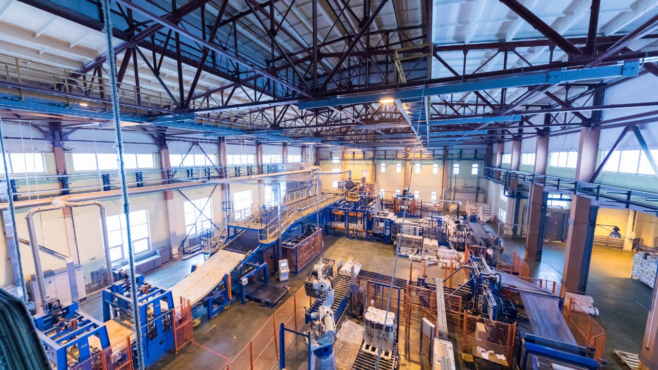 Vista ampla de uma fábrica com máquinas industriais, esteiras e linhas de produção em funcionamento.